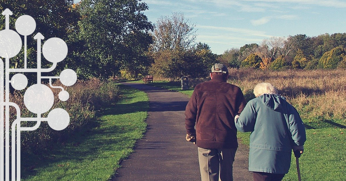Para seniorów spaceruje na tle terenów wiejskich.