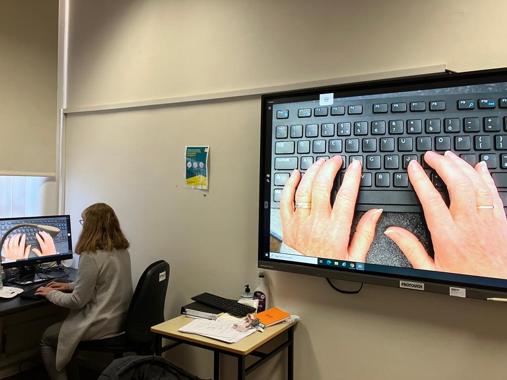 A picture of a teacher demonstrating how to use a keyboard using a visualizer.