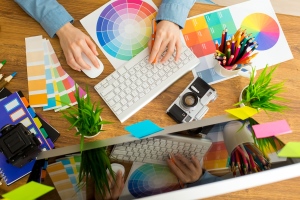 A young graphic designer's hands using a computer and surrounded by colour charts