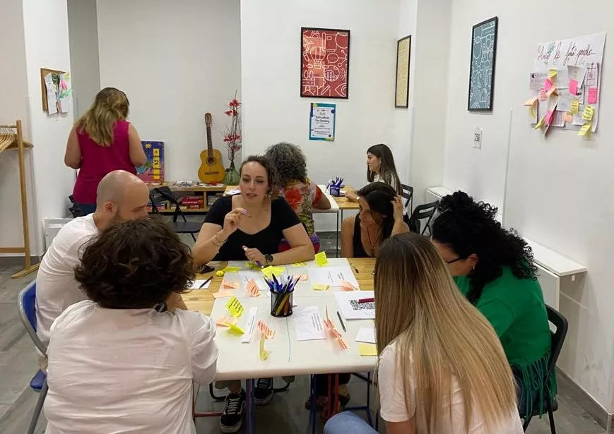 9 people discussing arounf tables with big white papers and colourful posti-it notes.