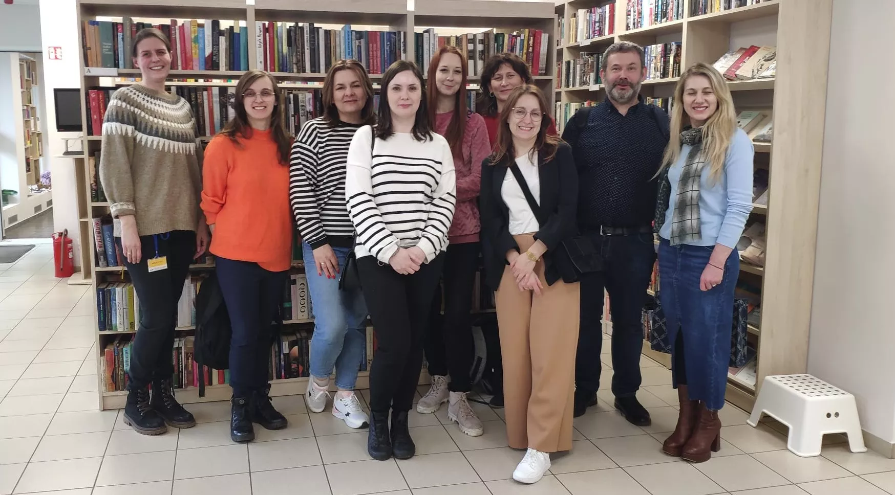 Spotkanie zapoznawcze bibliotekarzy z Polski i Litwy Grupa 9 osób dorosłych na tle półek z książkami.