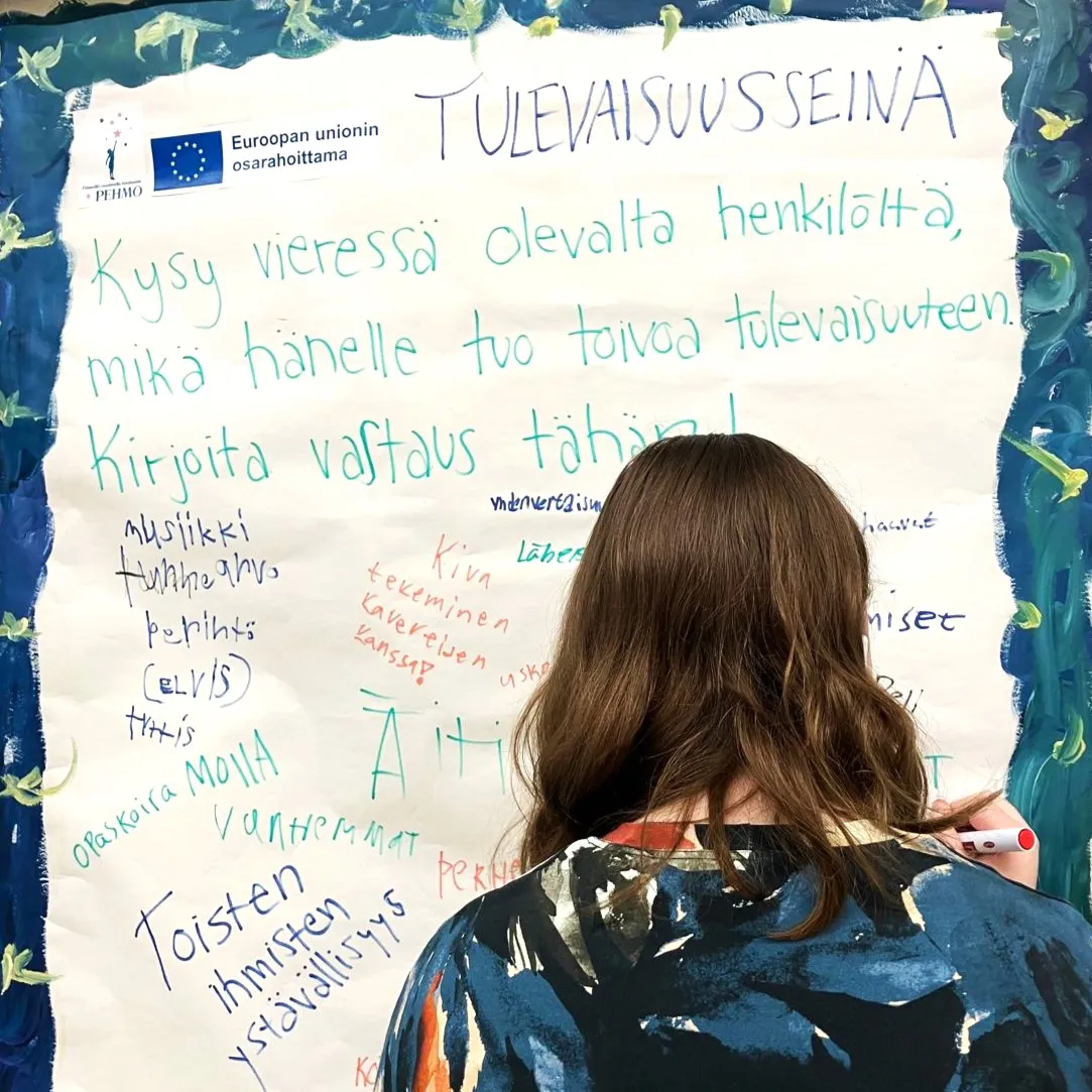 Henkilö kirjoittaa tekstejä fläppipaperille, jossa on otsikko "Tulevaisuusseinä".