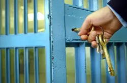 Hand unlocking the door to a prisoner's cell.