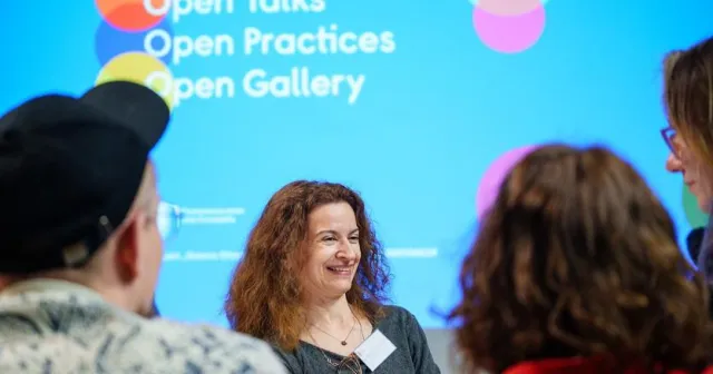 Zdjęcie. Kobieta siedzi obok napisu: Open Talks, Open Practices, Open Gallery.
