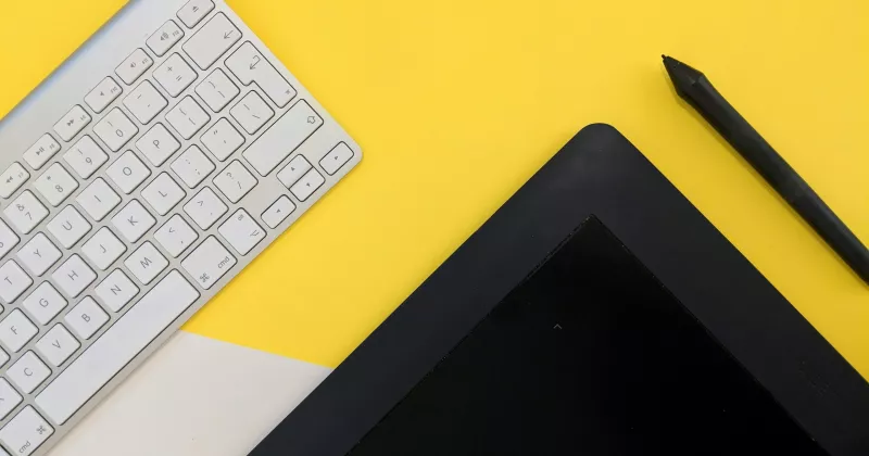 Tangentbord och skärm på bord med gul bakgrund.